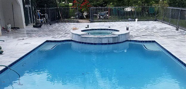 Swimming pool with spa, blue water, stone patio, and fenced backyard.