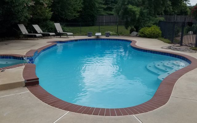 Swimming pool with turquoise water, brick border, and concrete patio. Lounge chairs are visible.
