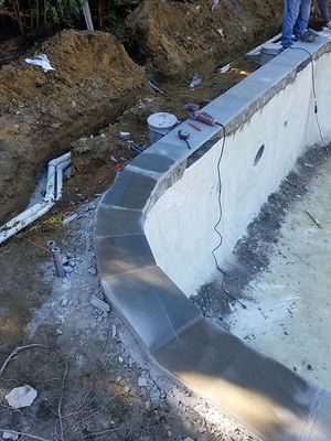 Construction of a curved pool edge with concrete, tools, and a person.