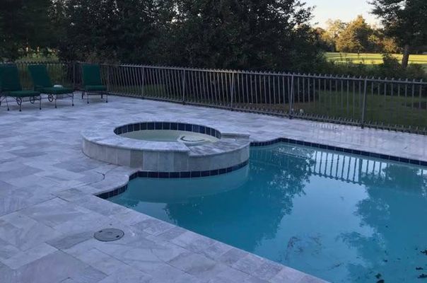 Pool and hot tub with gray tile surround, metal fence, and green chairs.