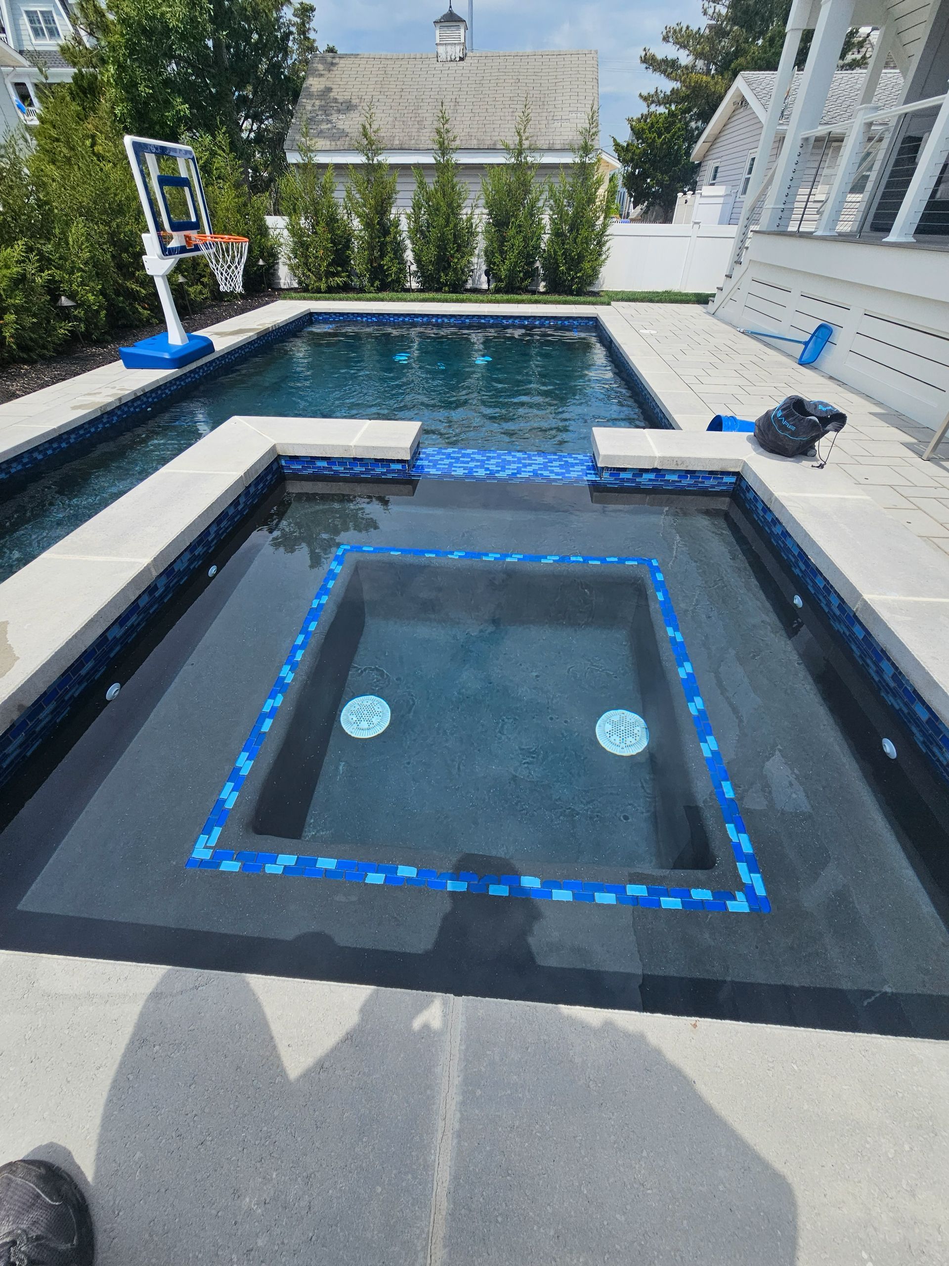 Pool and spa with blue tile accents and steps. Sunny outdoor setting.