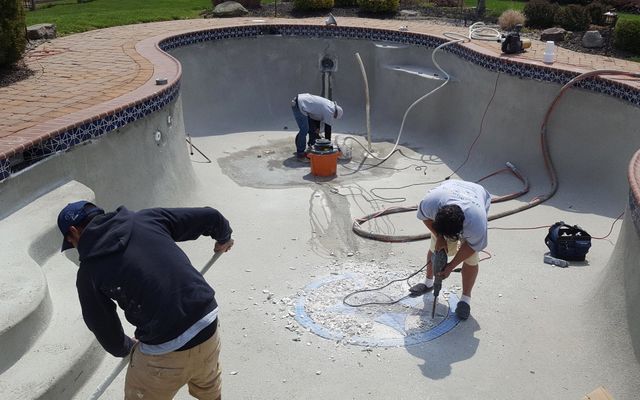 Men working in an empty swimming pool, removing old tiles and preparing the surface for renovation.