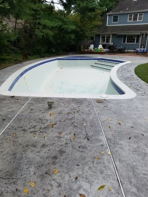 Empty outdoor swimming pool with concrete deck and a two-story house in the background.