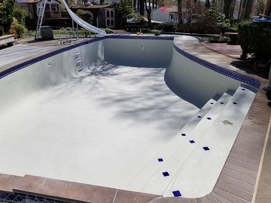 Empty swimming pool, painted white, with blue tile trim and steps. Outdoors, sunny day.