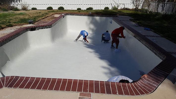People working inside an empty, rectangular pool, painting the interior.