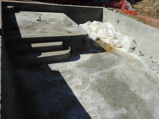 Concrete swimming pool under construction with steps and a shallow area.