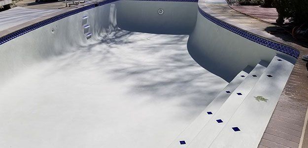 Empty swimming pool with white interior and blue tiled border, steps on the side.