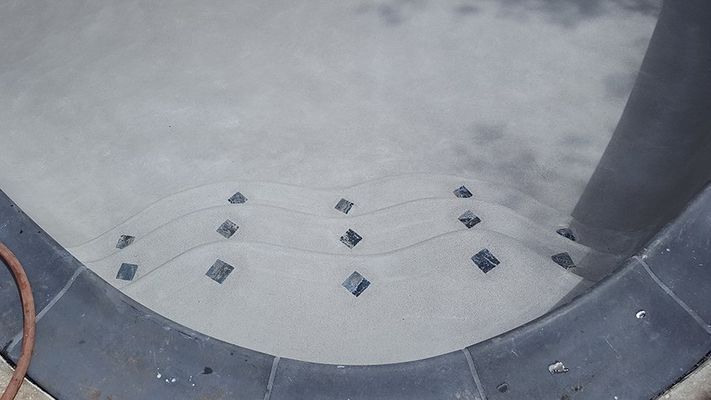 Pool steps with dark trim and inlaid dark diamond tiles. Gray textured surface.