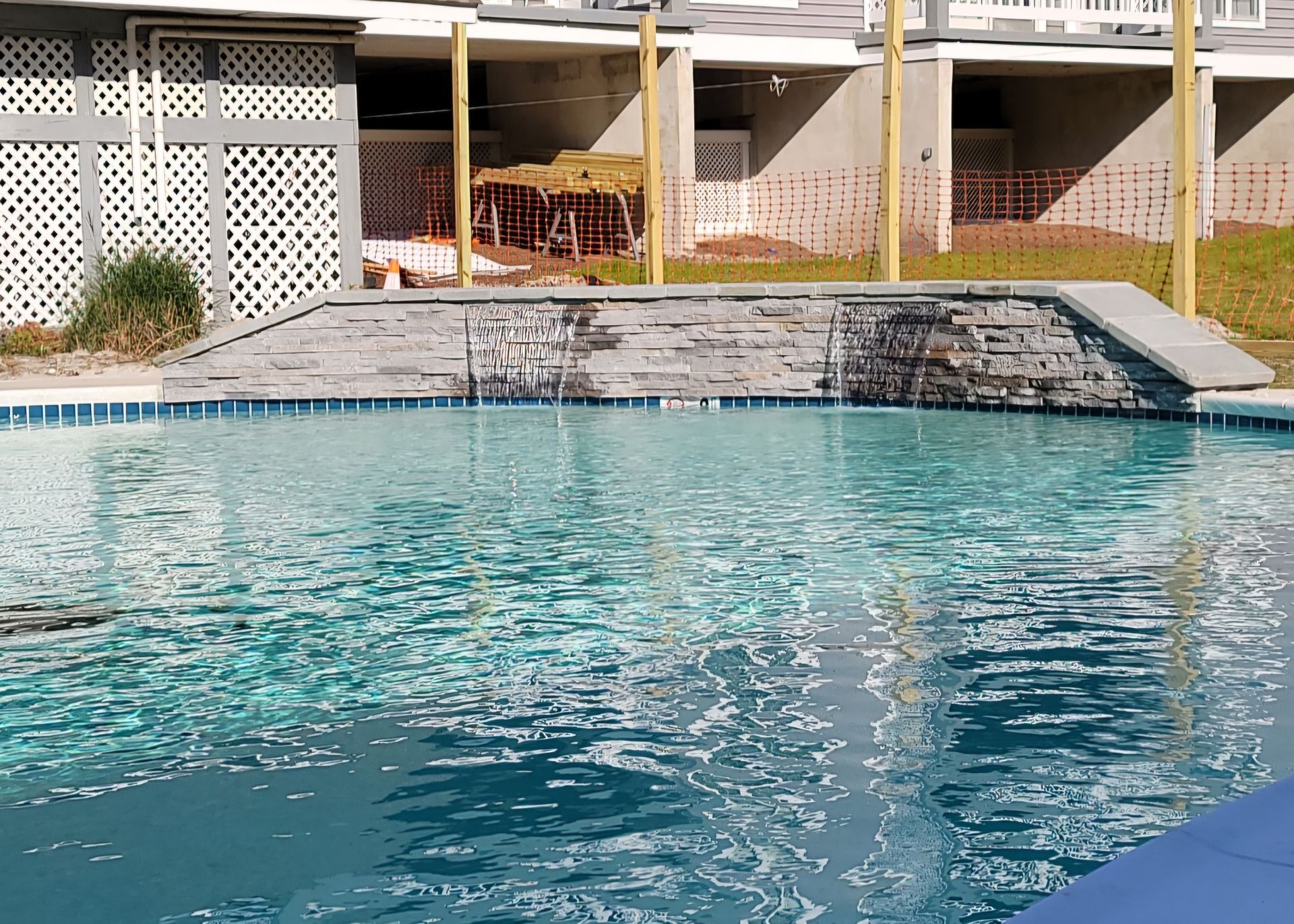 Pool with cascading waterfall feature and buildings in the background. Blue water and gray stone.