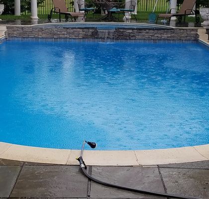 Rain falling into a blue swimming pool with a stone patio and raised stone spa.
