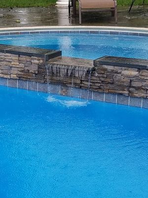 Pool with waterfall feature and stonework. Blue water with a chair visible in background.