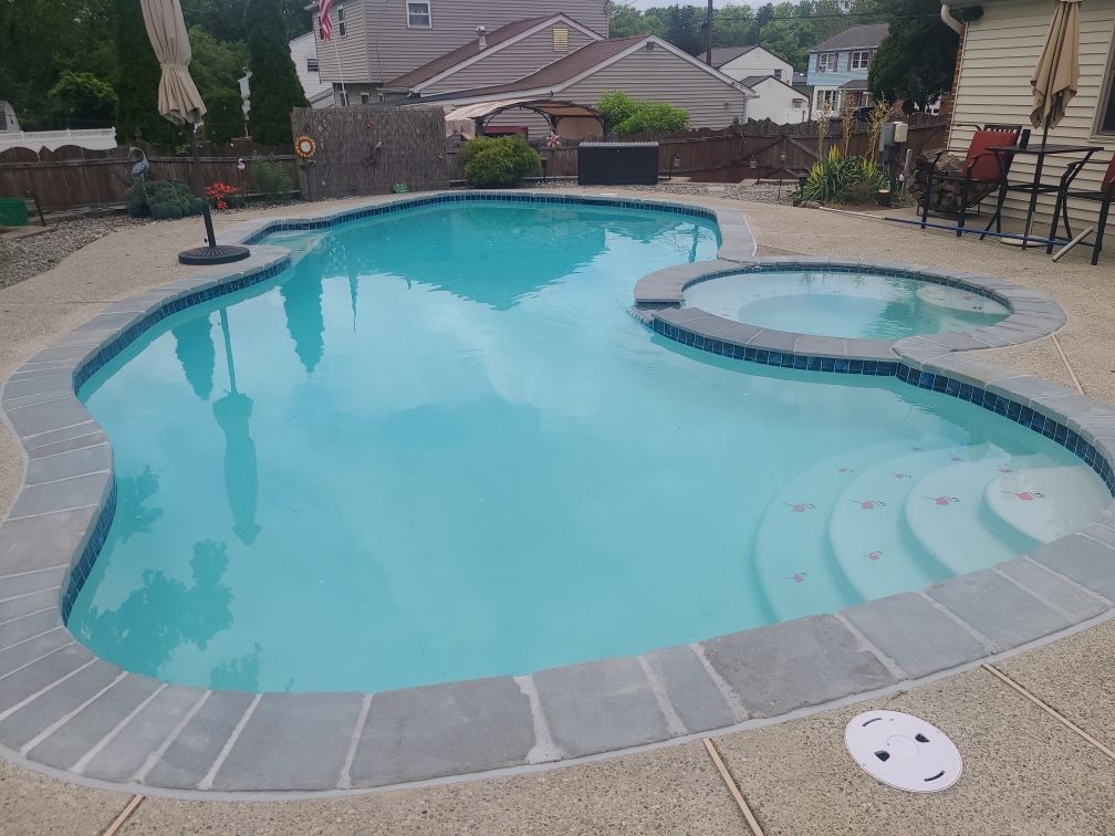 Swimming pool and hot tub with blue water, surrounded by a gray stone border and concrete patio.