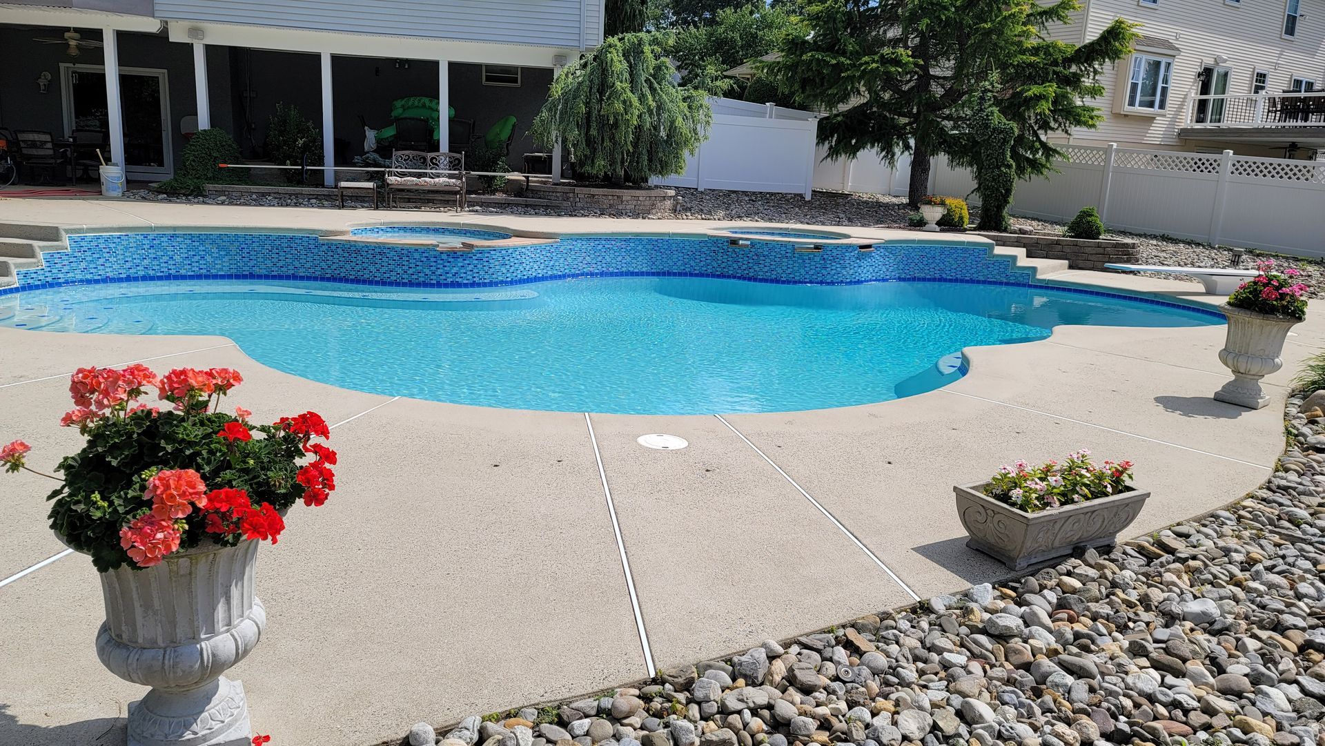 Swimming pool with blue tile interior, surrounded by a concrete patio and landscaping.