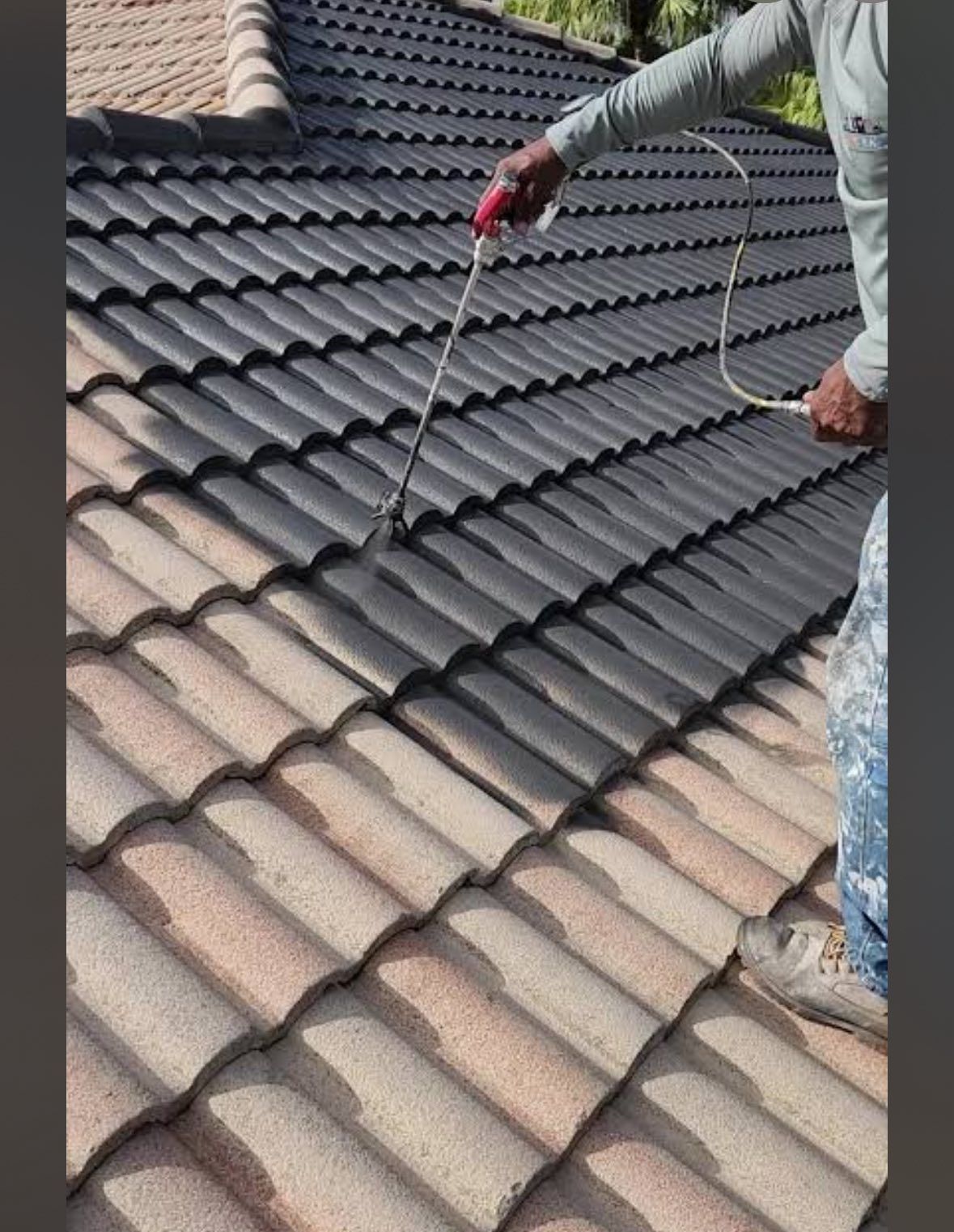 Person spray-painting a tiled roof from brown to dark gray.
