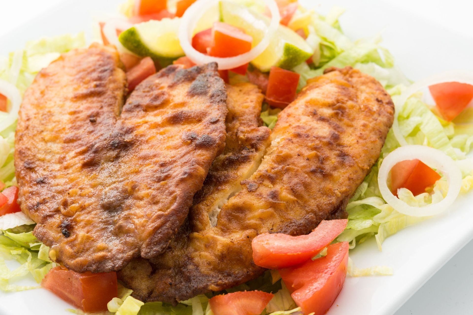 Fried fish fillets with chopped tomatoes, lettuce, and onion rings.