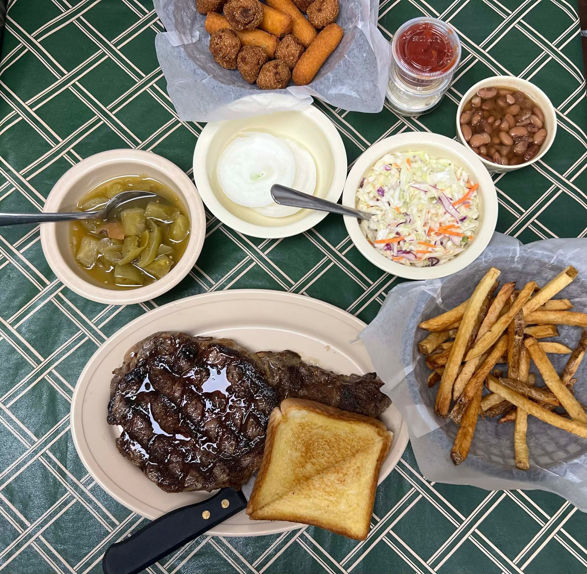 Steak dinner on checkered tablecloth with sides of beans, slaw, and fries.