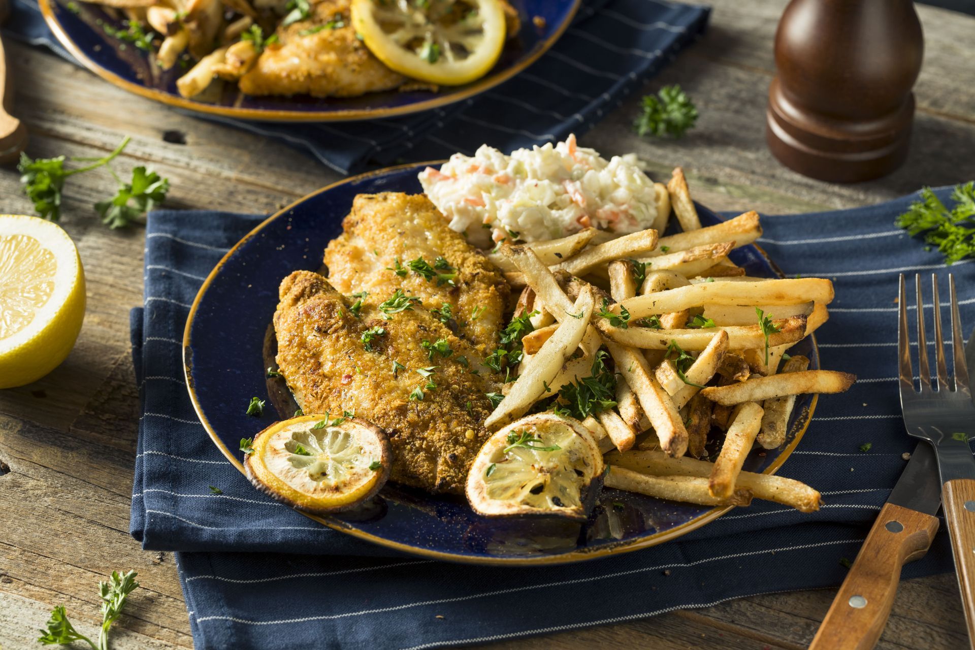 Fried fish with french fries, coleslaw, and lemon slices on a blue plate.