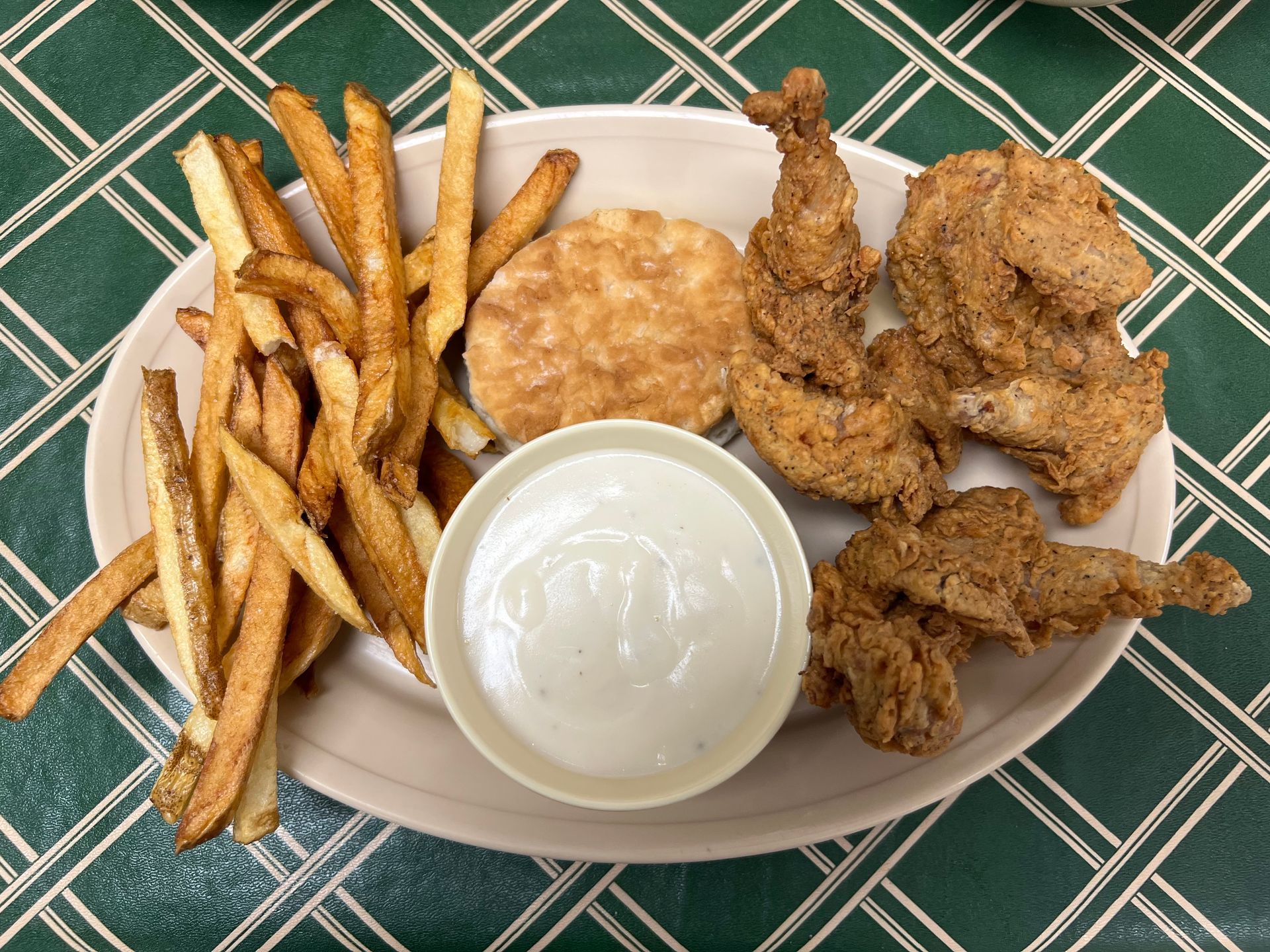 Plate of fried chicken, fries, biscuit, and gravy on a green patterned tablecloth.