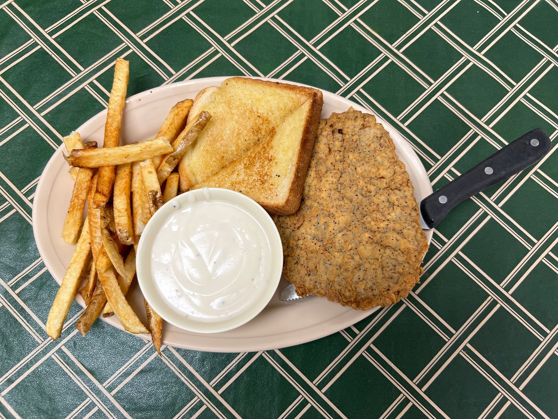 Chicken fried steak with fries, toast, and gravy on a beige plate.