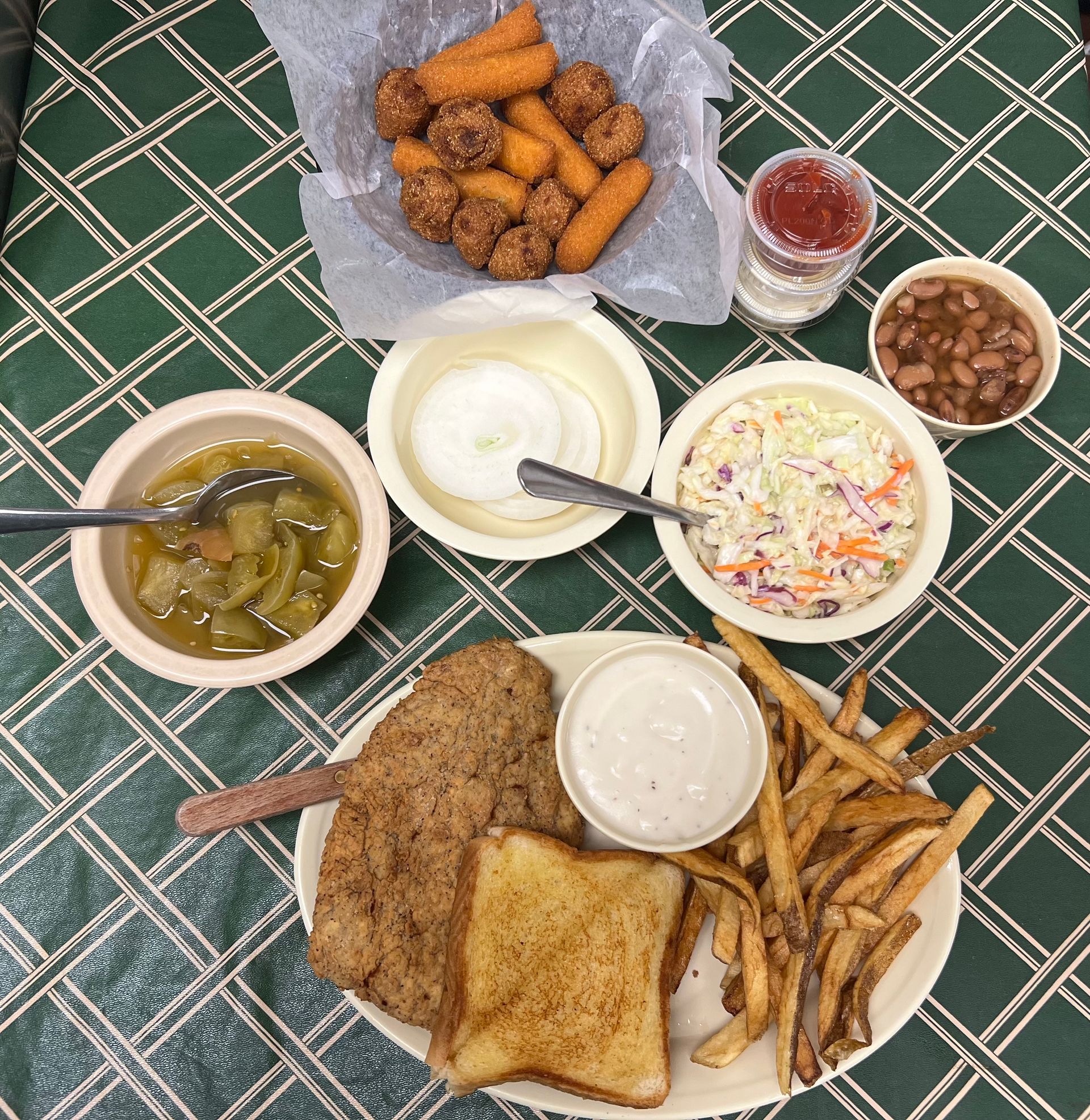 Meal with meat, fries, bread, sides including coleslaw, beans, onions, and dipping sauce.
