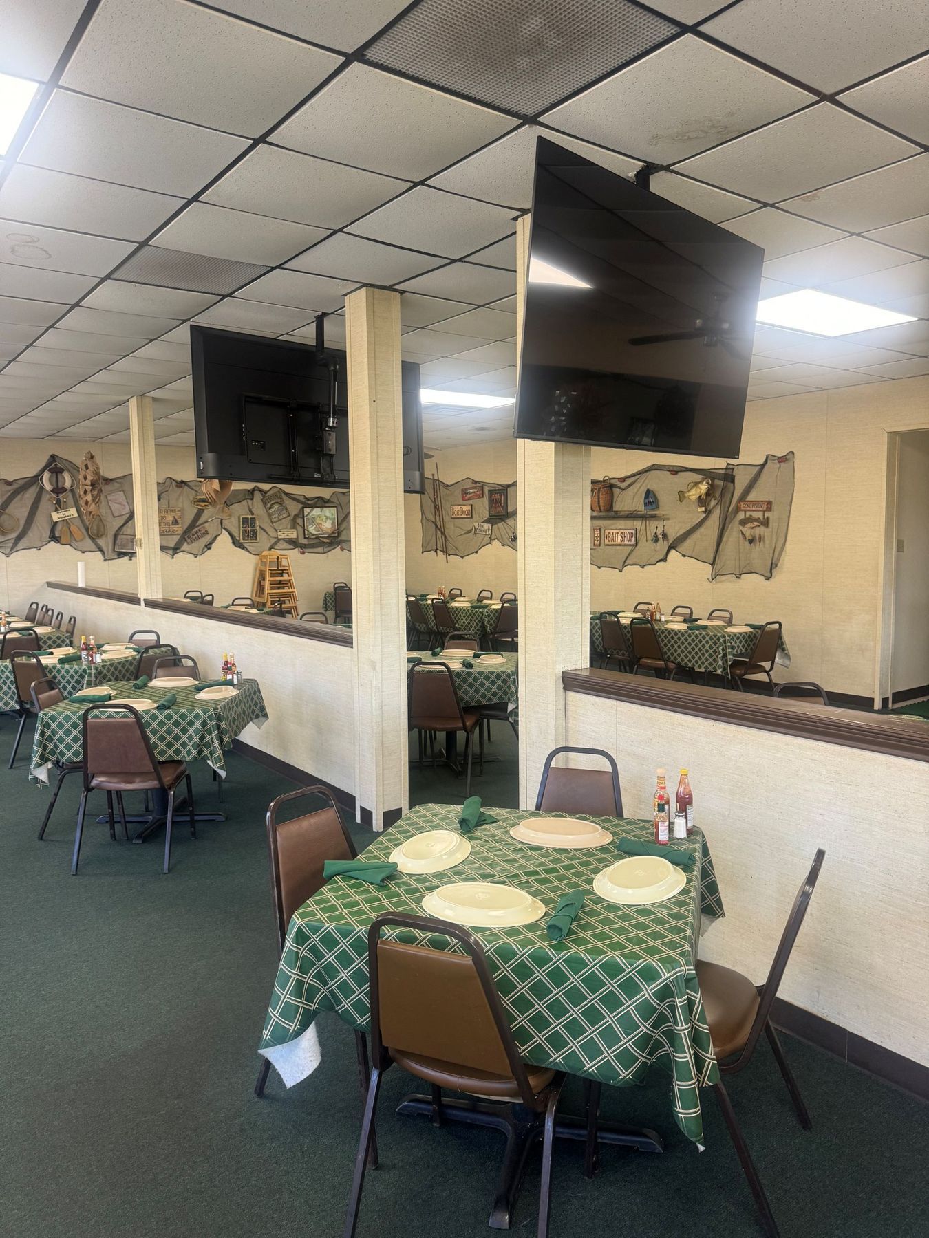 Restaurant interior with green tablecloths, brown chairs, and TVs on the walls.