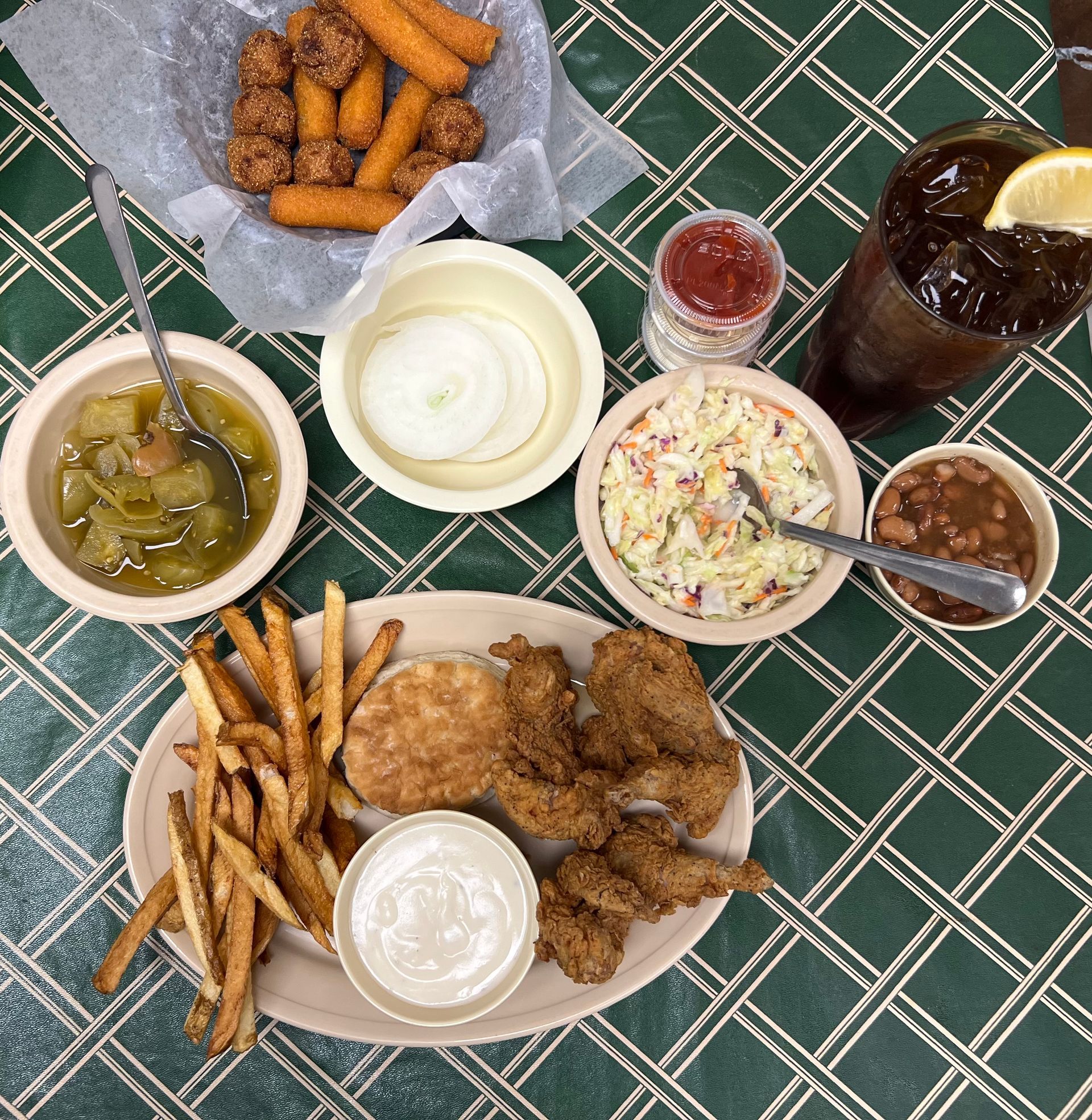 Fried chicken platter with sides like fries, beans, coleslaw, and a drink.