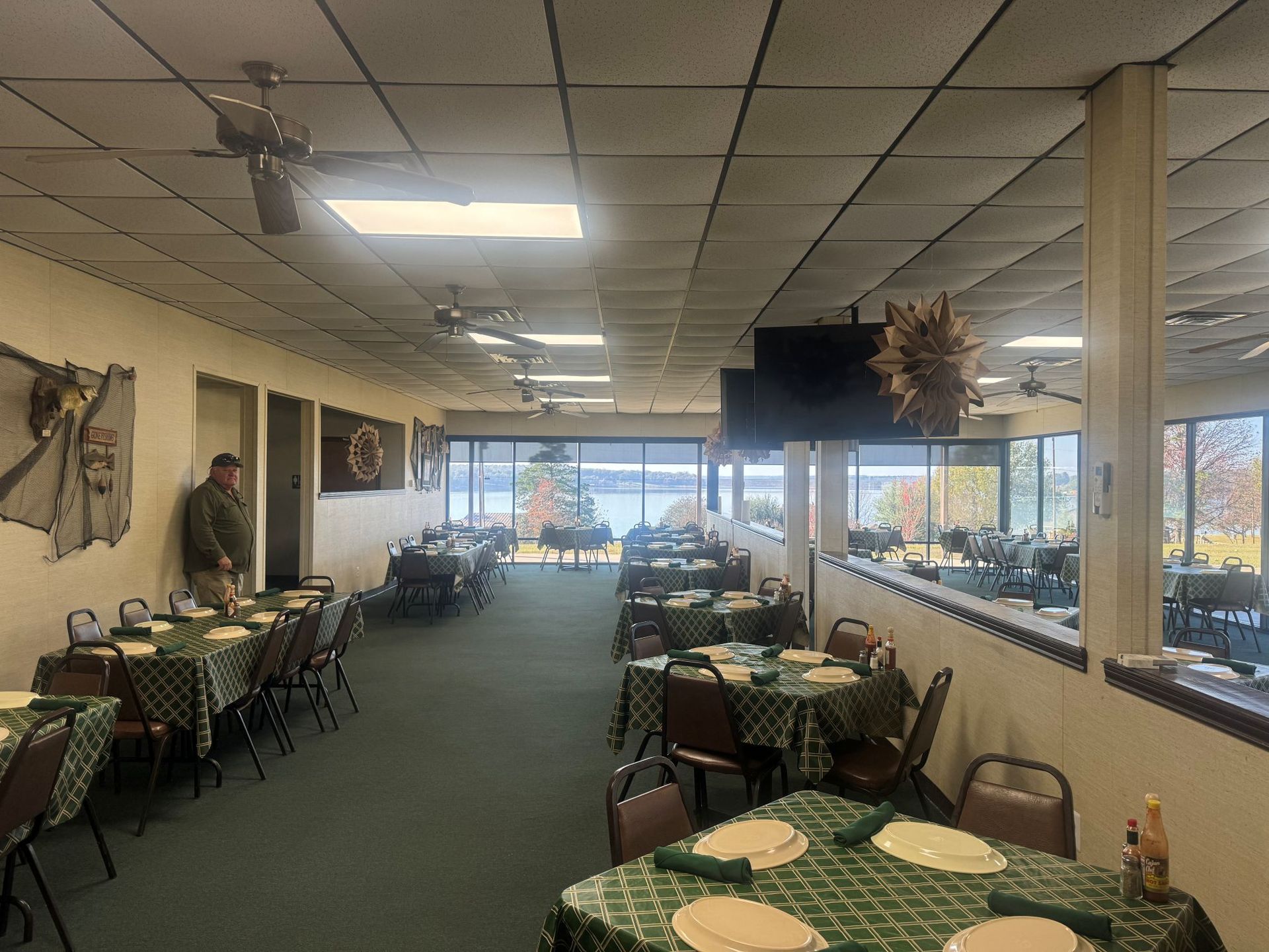 Restaurant interior with tables set for diners and large windows overlooking a lake.