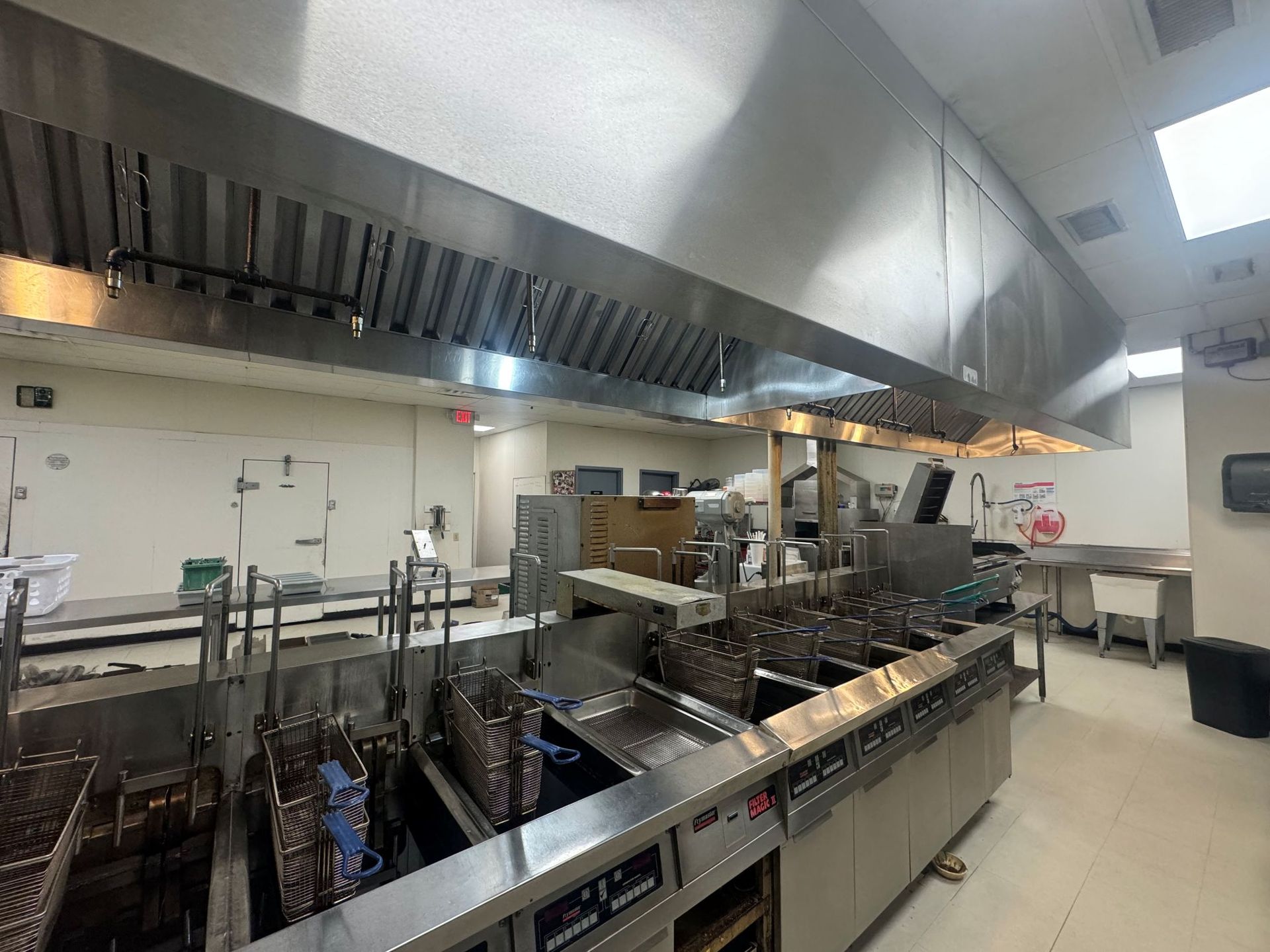 Commercial kitchen with stainless steel equipment including fryers and a ventilation hood.