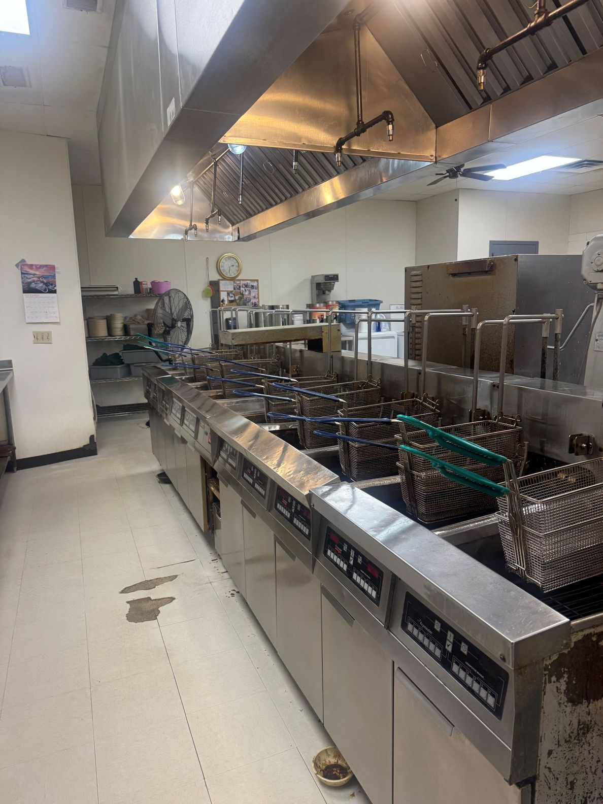 Commercial kitchen with stainless steel fryers, exhaust hood, and industrial equipment.