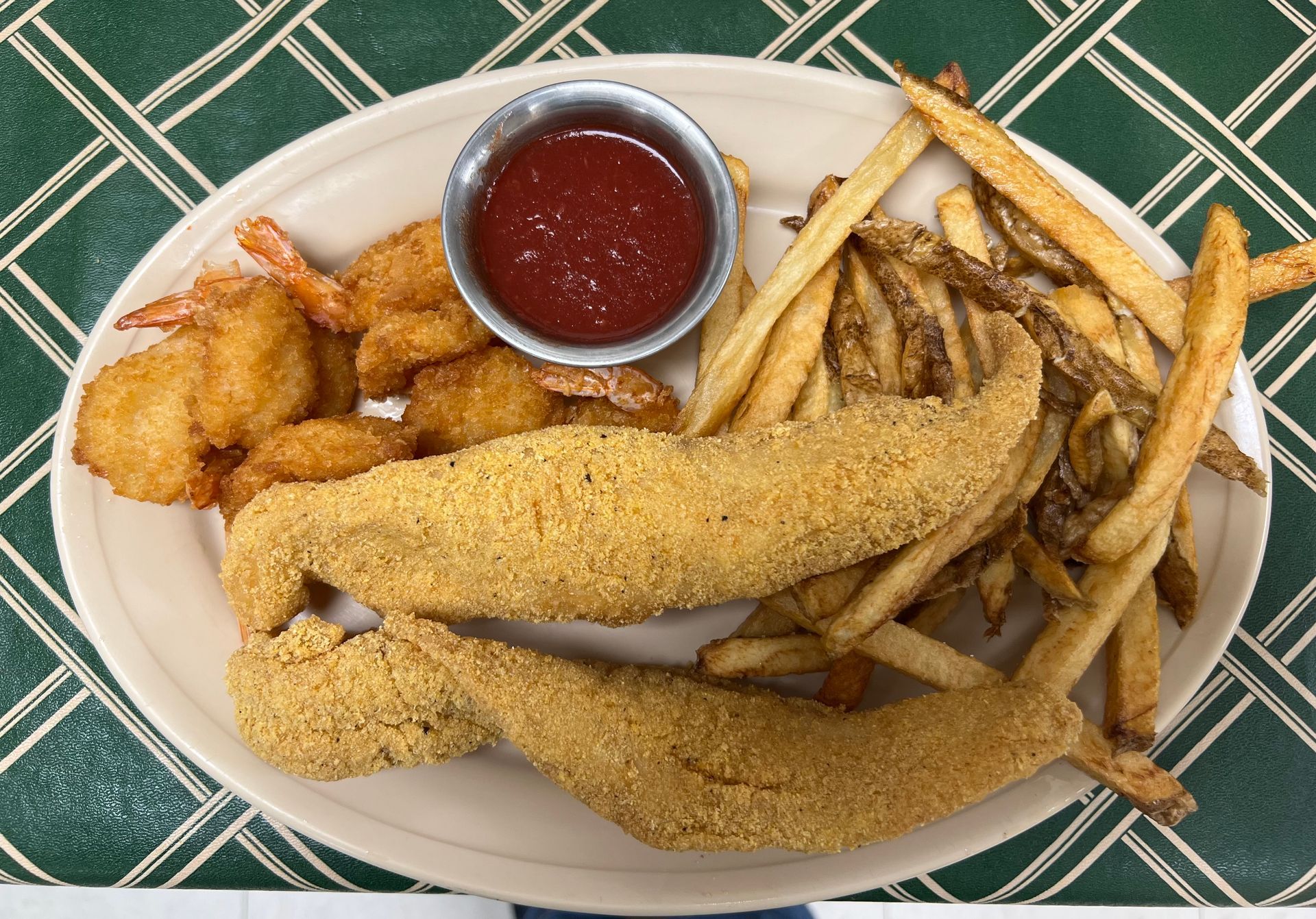 Fried fish, shrimp, and fries on a plate with ketchup.