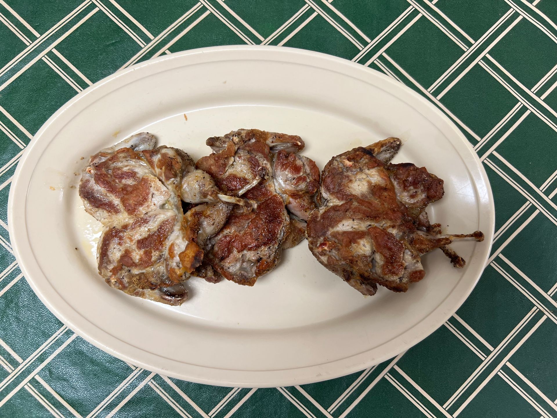 Plate of cooked quail on a green checkered tablecloth.