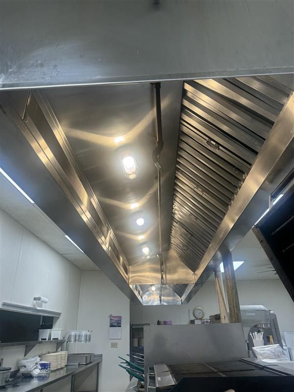 Commercial kitchen ceiling with stainless steel exhaust hood, lights, and equipment.