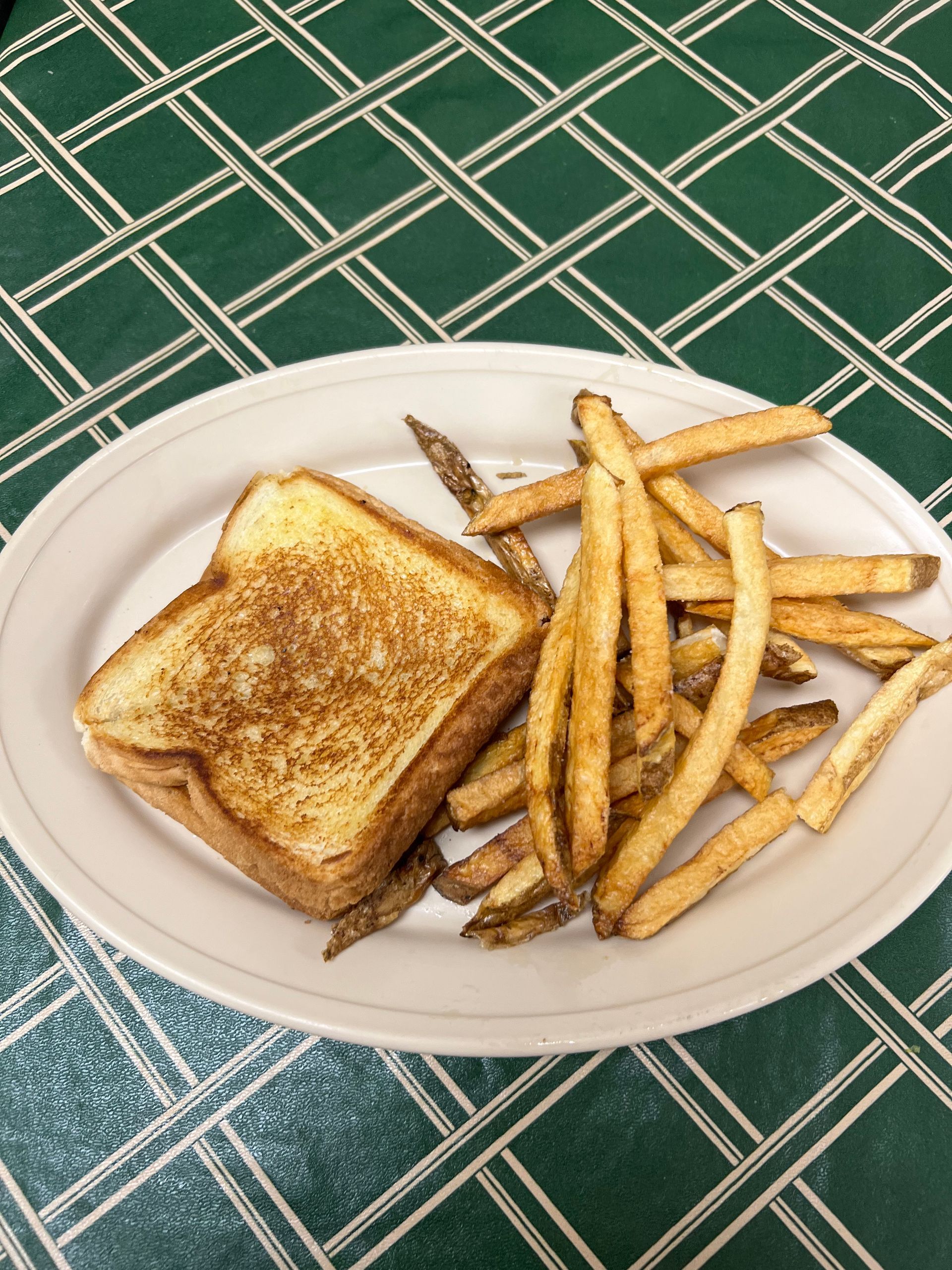Grilled cheese sandwich and fries on a white plate, atop a green patterned tablecloth.