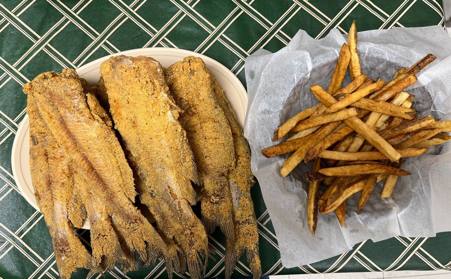 Fried fish fillets on a plate next to a basket of french fries on a green patterned surface.