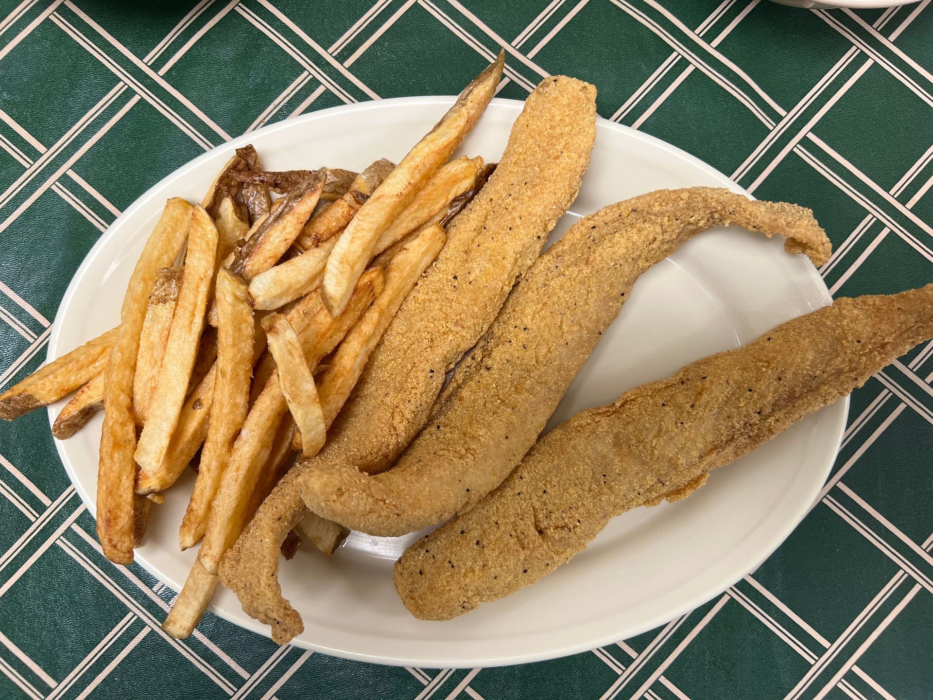 Plate of fried fish and french fries on a green and white checkered surface.