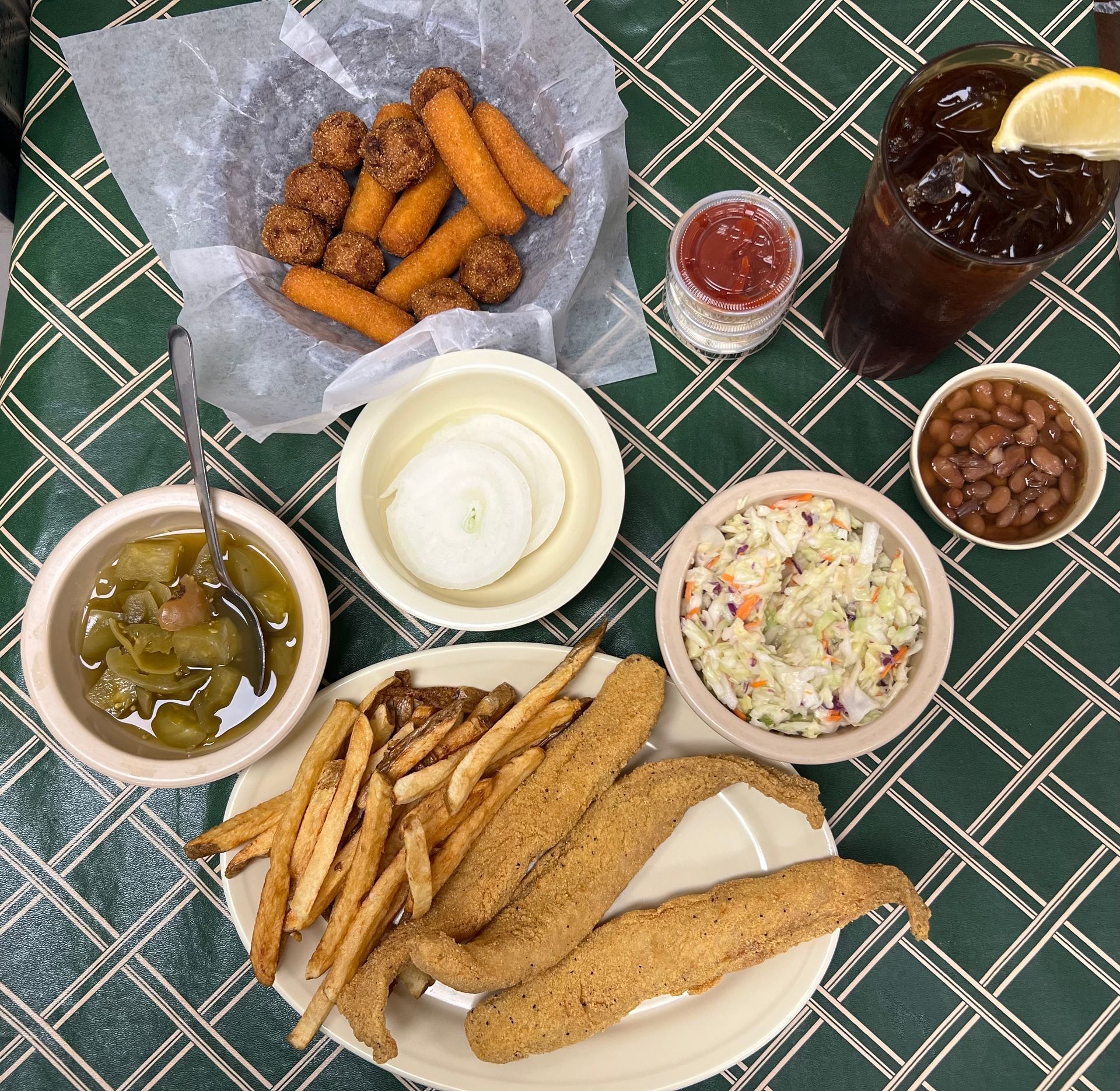Fried fish platter with sides, including fries, coleslaw, beans, pickles, and iced tea.