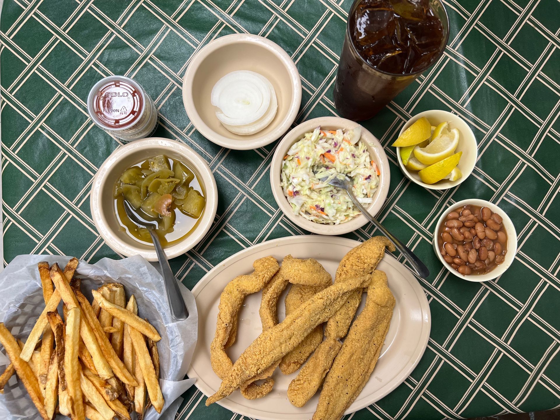 Fried catfish meal with sides: fries, coleslaw, beans, pickles, onions, lemons, and iced tea.