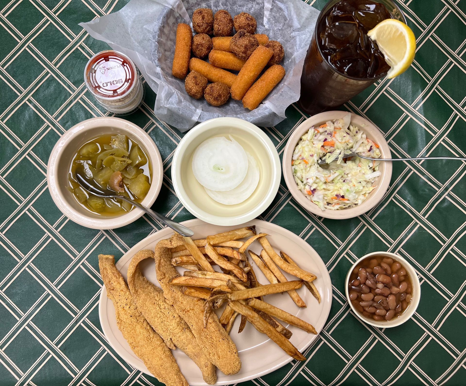 Fried catfish with fries, coleslaw, beans, hushpuppies, tea, and pickles on a green tablecloth.