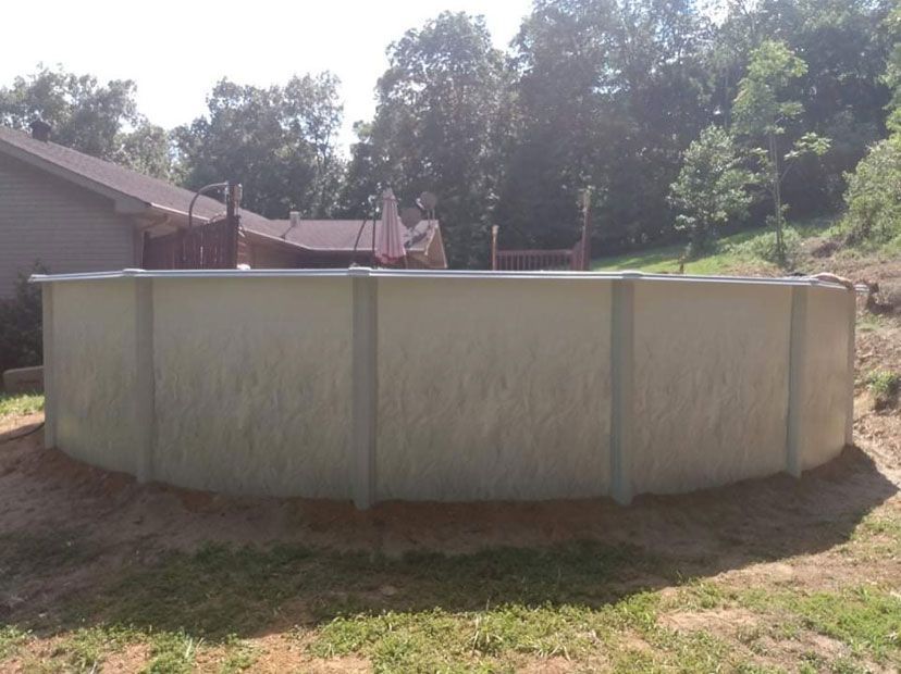 Above-ground pool, cylindrical shape, in a yard. Tan pool walls, surrounded by dirt, set next to a wooden deck.