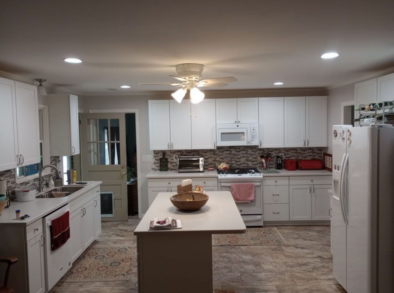 Bright white kitchen with a center island, white cabinets, stone backsplash, and stainless appliances.