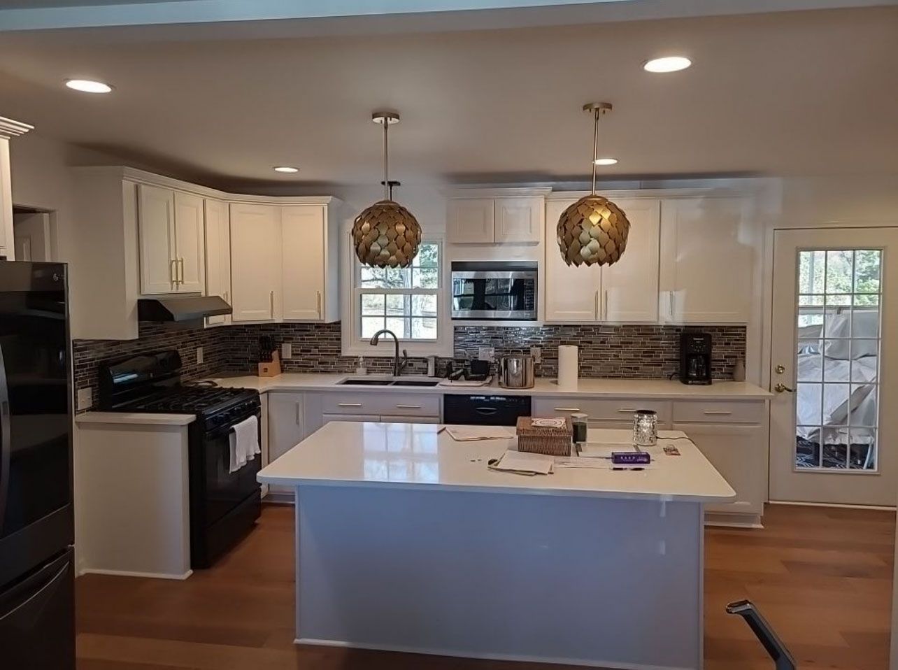 White kitchen with island, dark appliances, gold pendant lights, and tile backsplash.