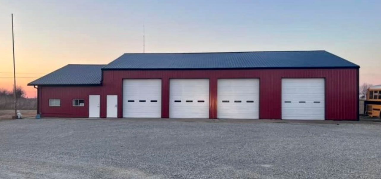 Red building with four garage doors and a black roof against an orange and blue sky.