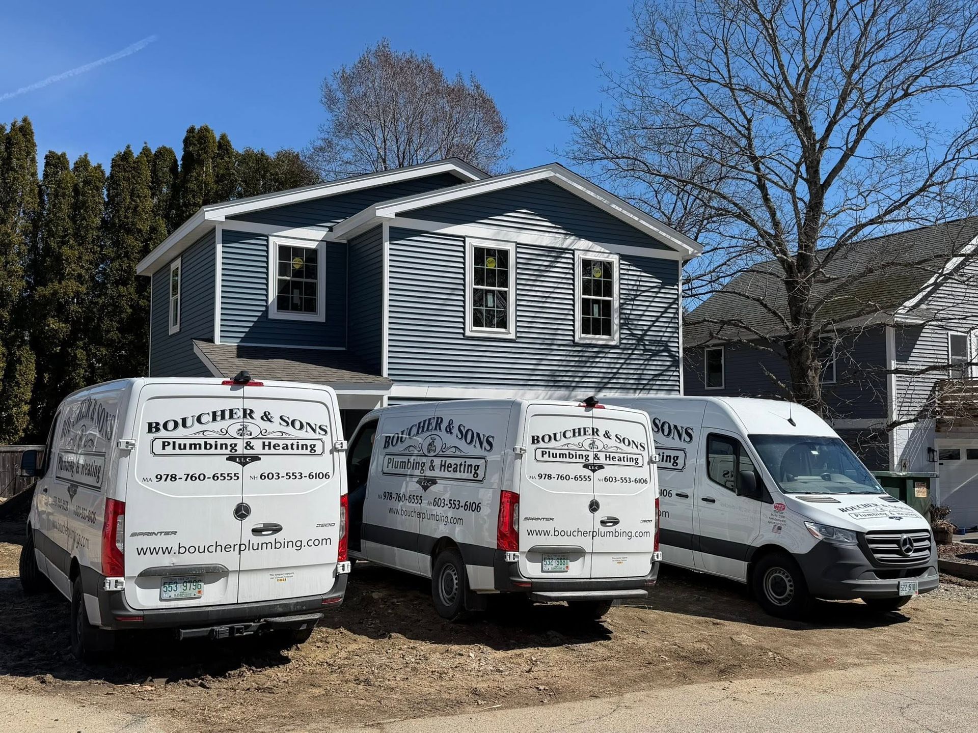 Blue house under renovation with three white work vans parked in front on a sunny day