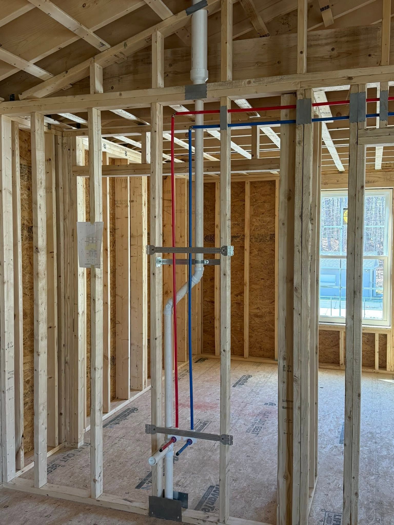 Unfinished house interior with exposed wood framing and a red-and-white ladder in the center.