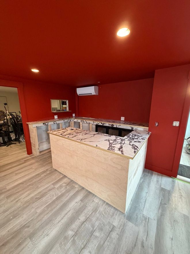 Red room with a central counter, microwave, and warm ceiling lights in a small shop or café.