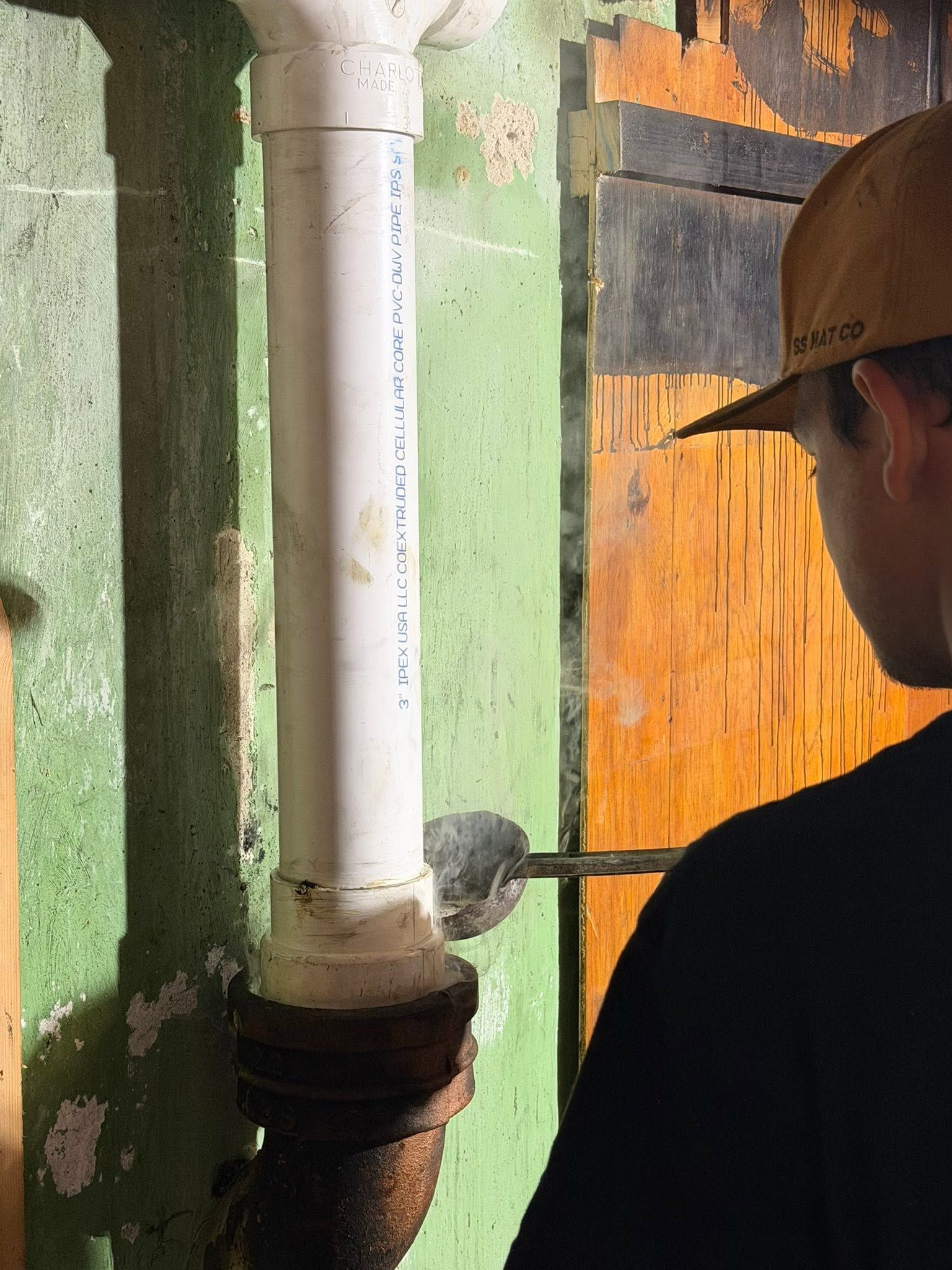 Worker inspecting a white pipe on a green wall with orange insulation panels nearby