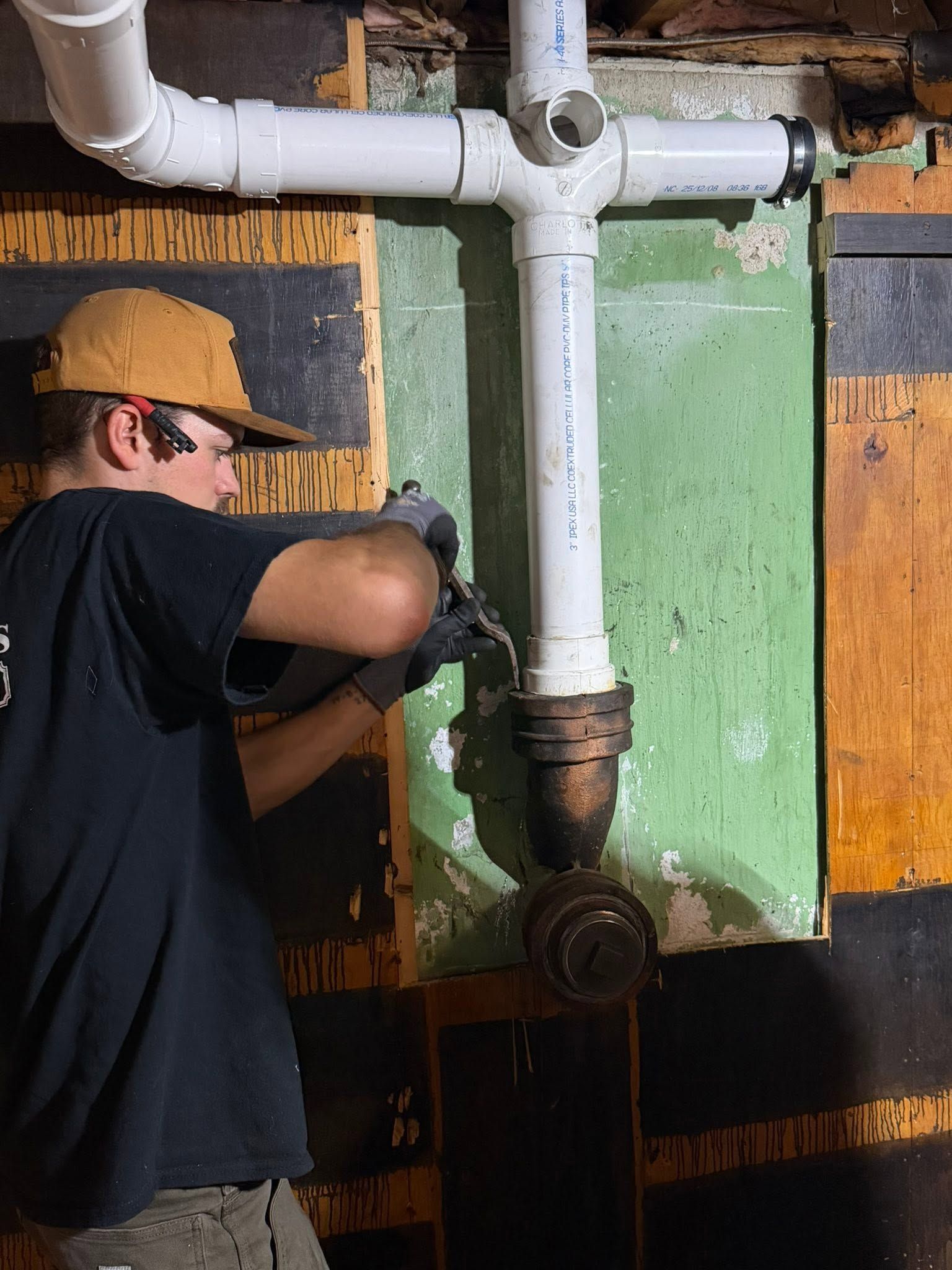 Worker in hard hat tightening a pipe valve on industrial plumbing with green and black wall panels.