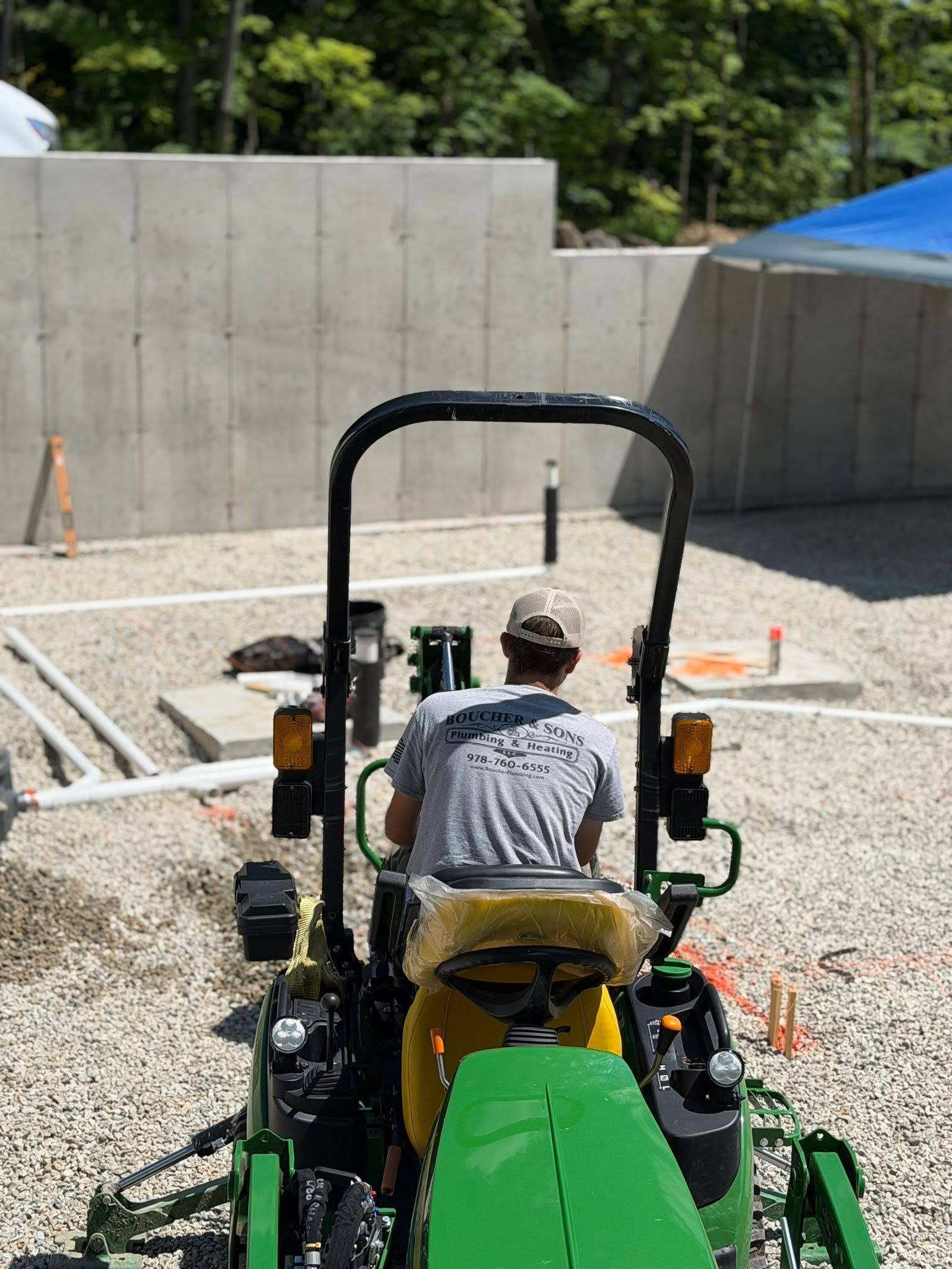 Person driving a green construction vehicle at an outdoor worksite with concrete walls and gravel