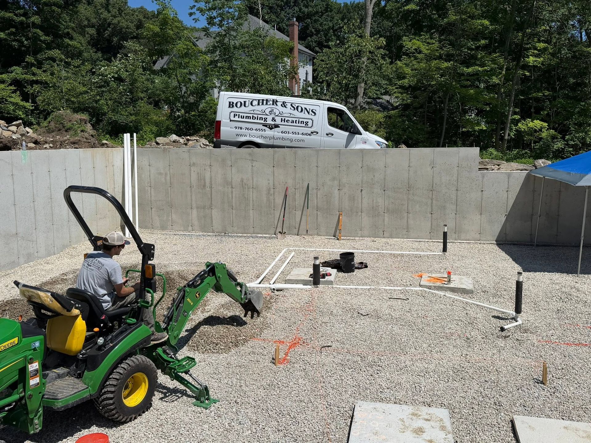 Green tractor on gravel beside a block wall at a construction site, with a white van behind it.