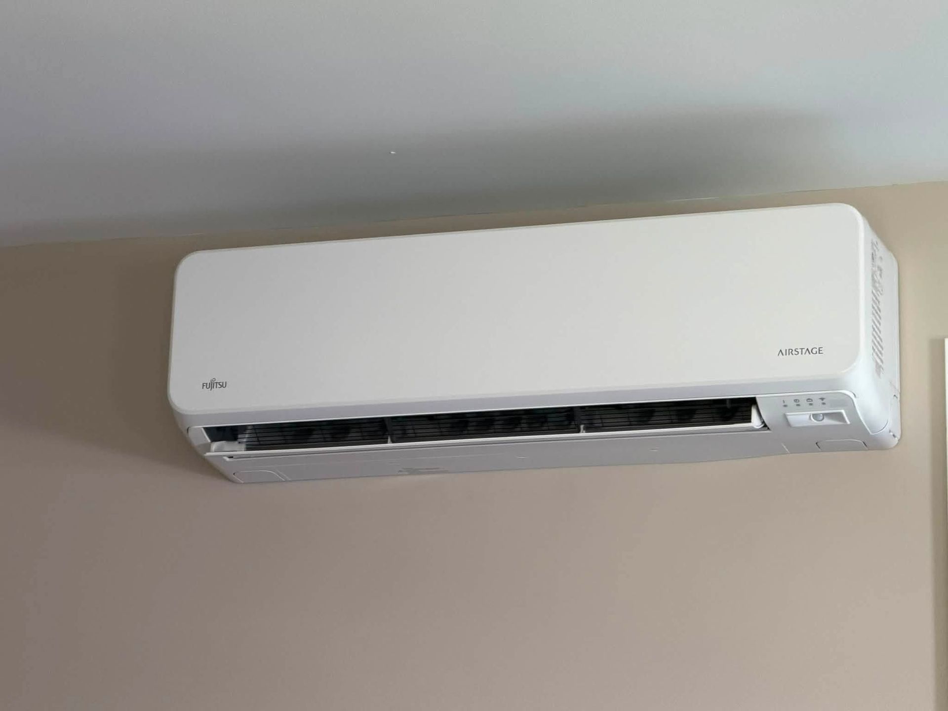 White wall-mounted air conditioner near the ceiling in a beige room